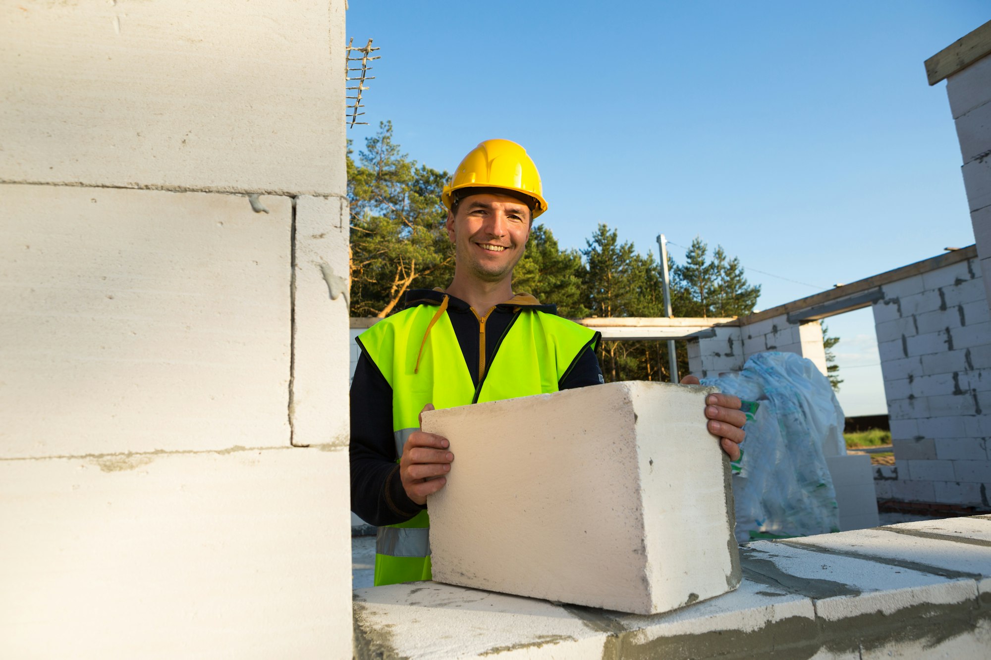 The builder holds a block of cellular concrete in his hands - the masonry of the walls