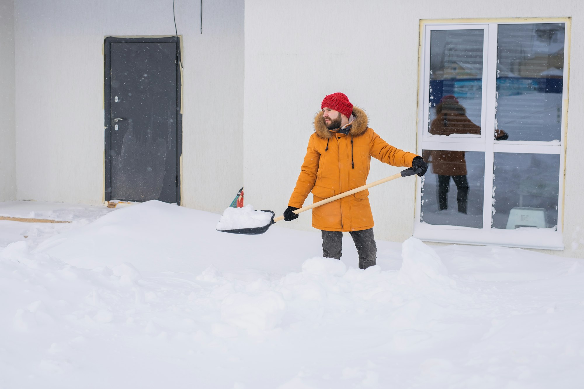 Young man clearing snow in his backyard village house with shovel. Remove snow from the sidewalk.